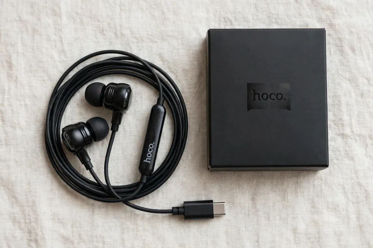 Flat lay of the coiled black Hoco M116 Type-C earphones beside minimal black Hoco retail packaging