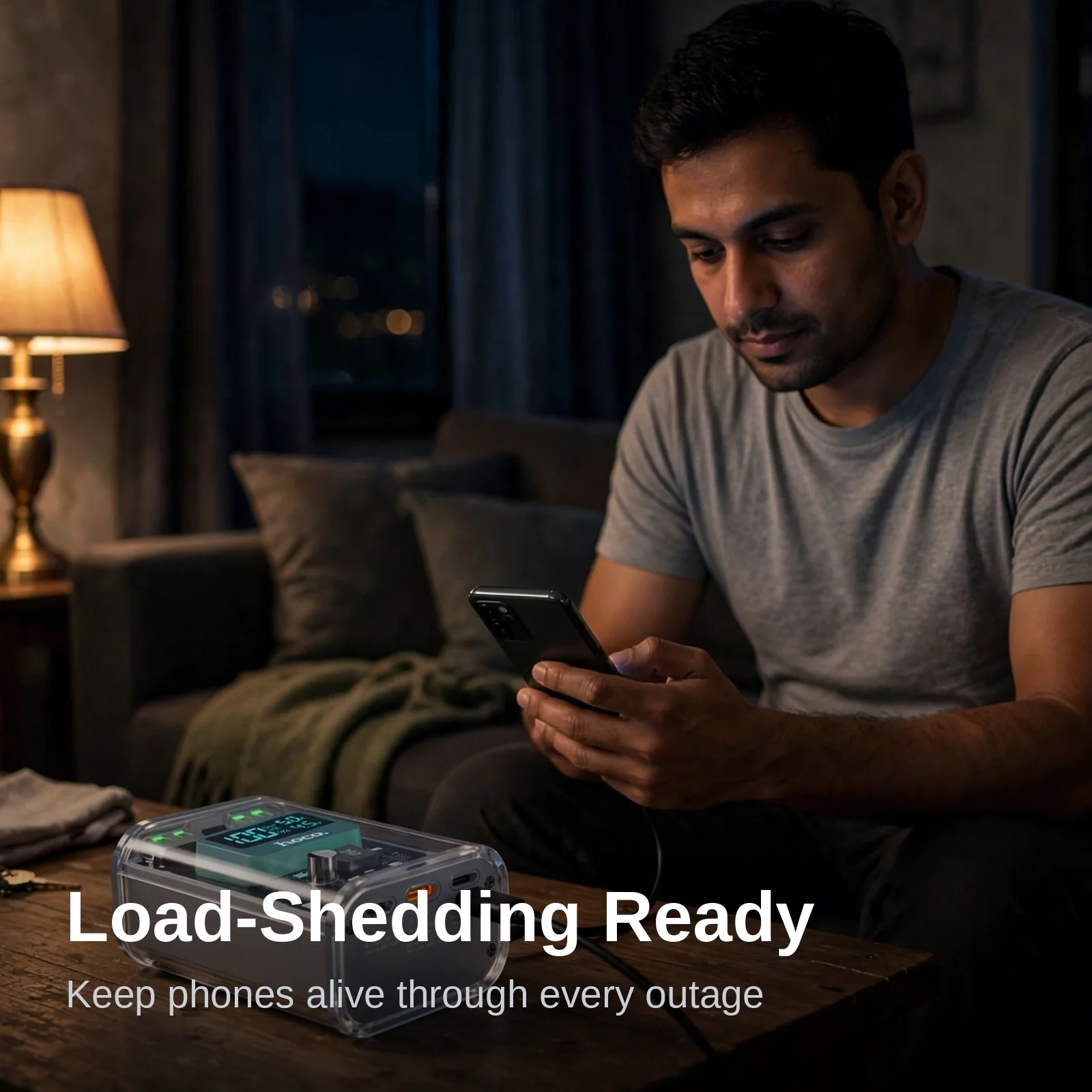 Man using his phone at home during a power outage with the Hoco J105 Crystal gray power bank on the table beside him